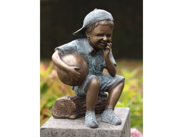 Skulptur aus Bronze sitzender Junge auf einem Baumstamm mit Ball im Arm