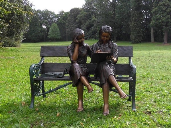Bronzeskulptur zwei sitzende Mädchen beim Lesen auf einer Bank mit Lehne